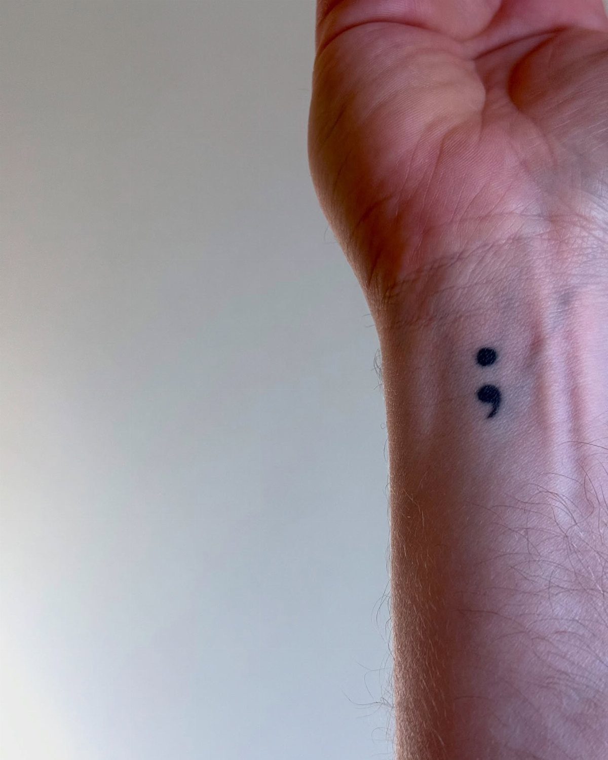 Small black semicolon tattoo on the inner wrist of a person.