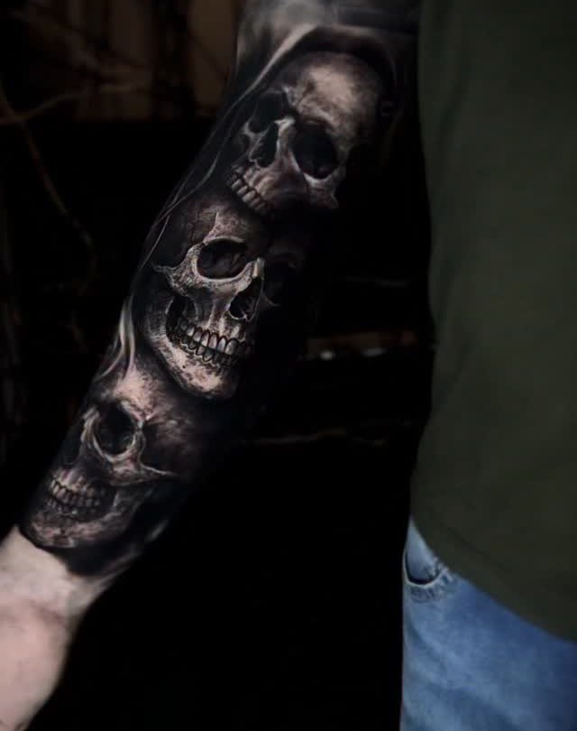 Detailed black and grey tattoo of three realistic human skulls on a forearm.