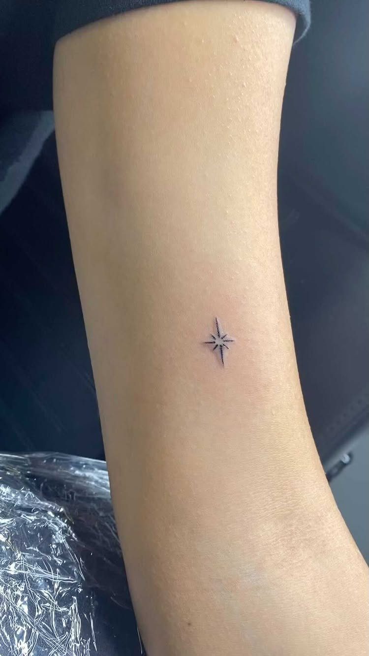 Small black four-pointed star tattoo on a person's inner forearm.