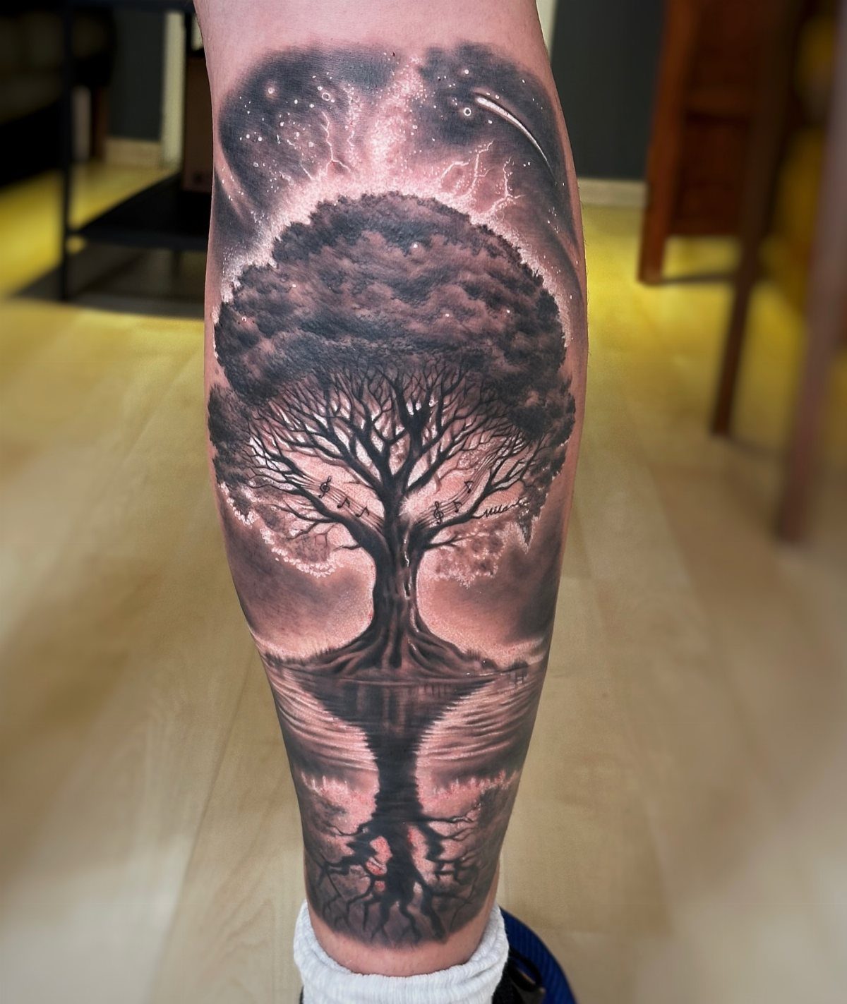 Tree of life tattoo on a leg with cosmic sky and water reflection