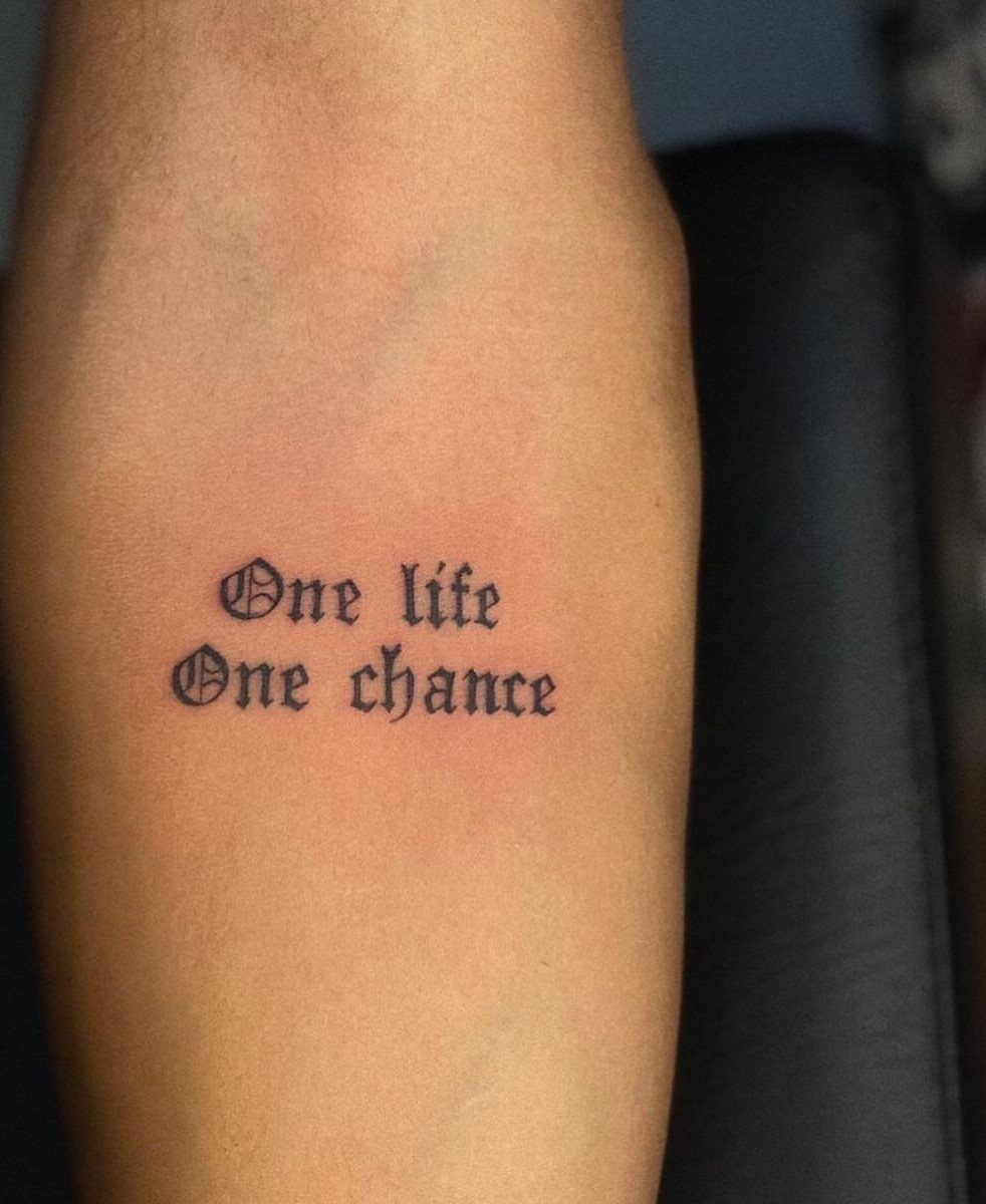 Black ink tattoo on a forearm reading One life One chance in gothic font