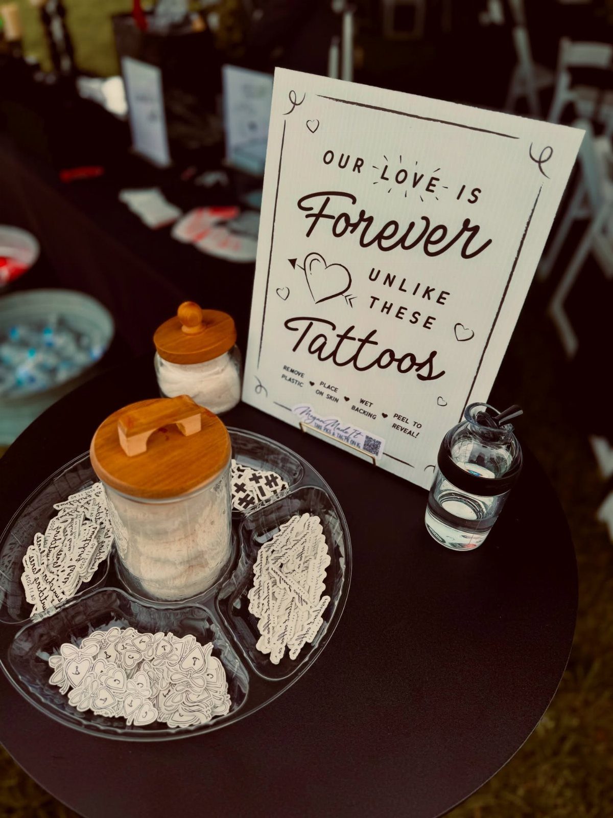 Temporary tattoo station with a sign, divided tray of tattoos, and glass jars.