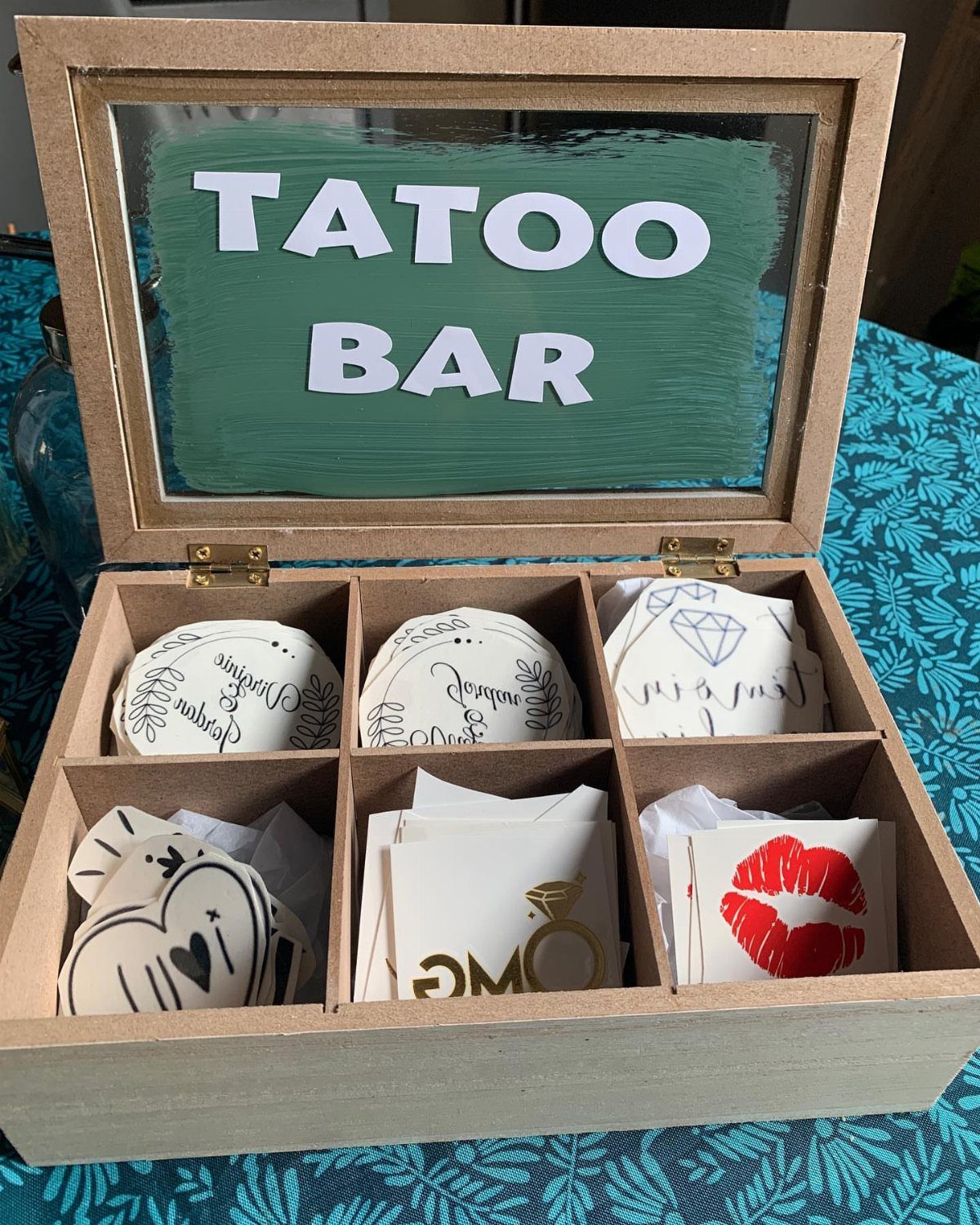 Wooden tattoo bar box with compartments holding various temporary tattoo designs.