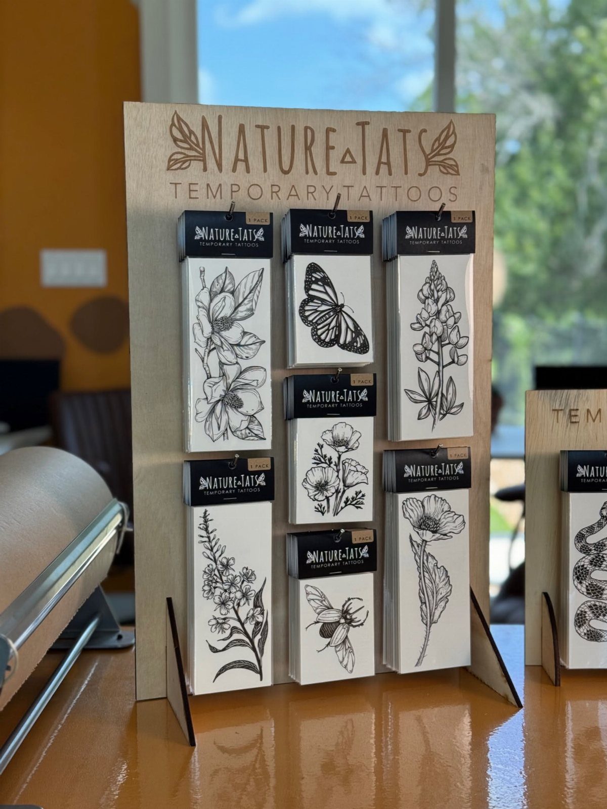 Wooden display board showcasing various nature-themed temporary tattoo packages with floral and insect designs.