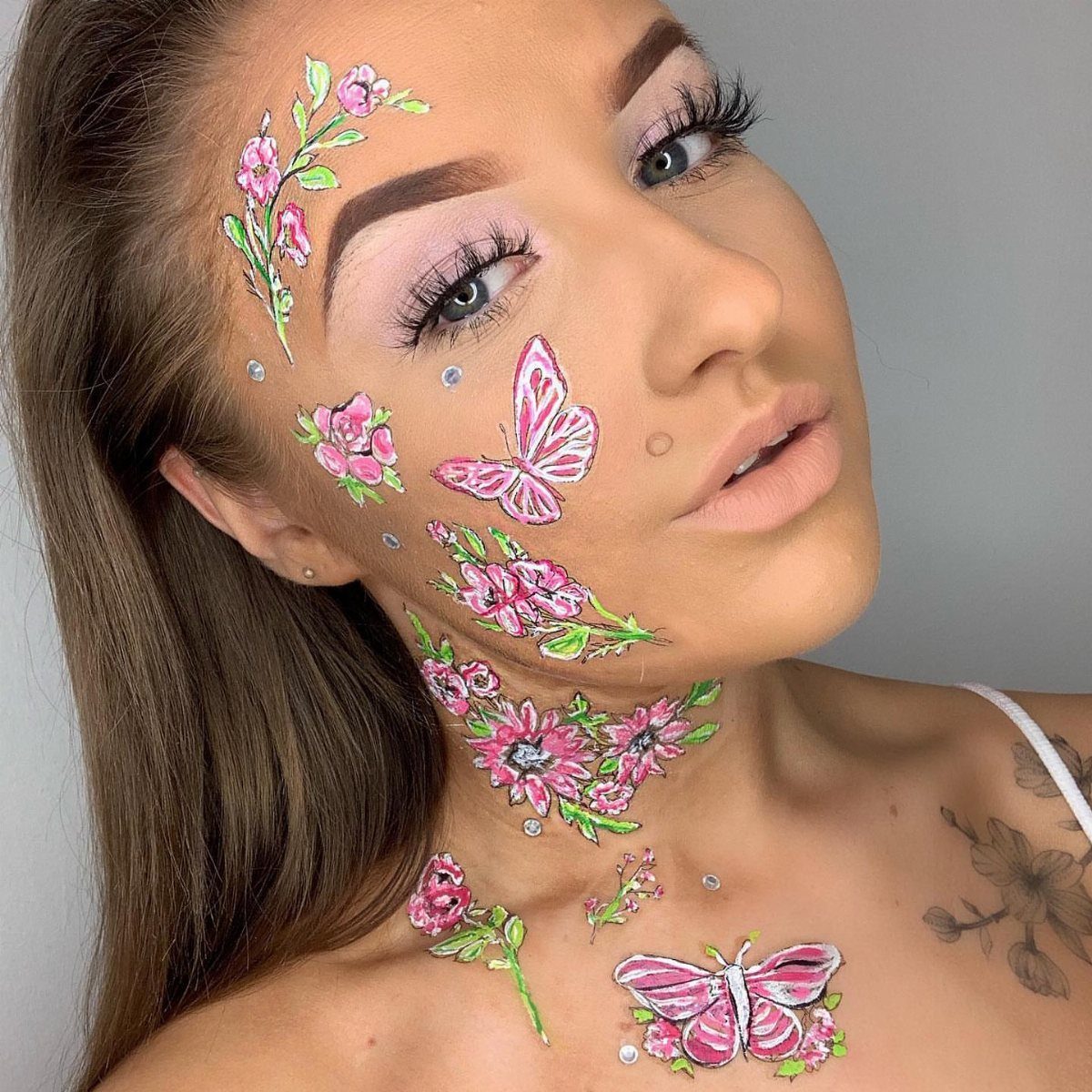 Woman with pink floral and butterfly temporary tattoos on her face and neck.