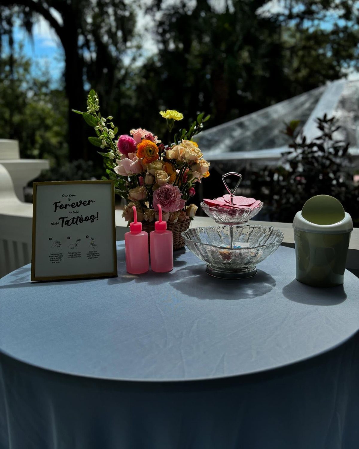 Temporary tattoo station on a blue table with flowers and a framed sign.