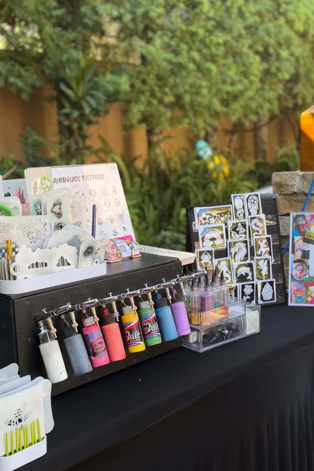 Airbrush tattoo supplies including colorful ink bottles and design sheets on a black table.