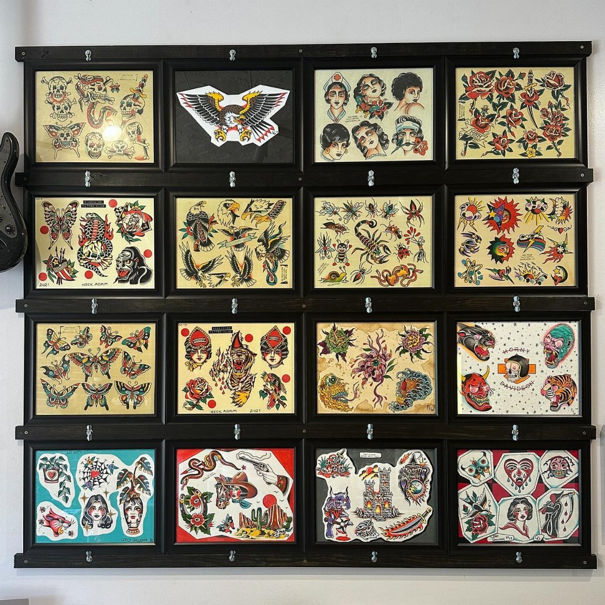 Black framed display grid showcasing various colorful temporary tattoo sheets on a white wall.