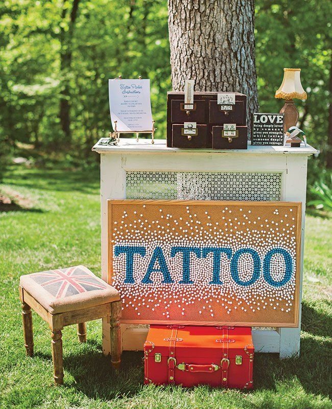 Large orange sign with blue TATTOO text leaning against a white cabinet outdoors.