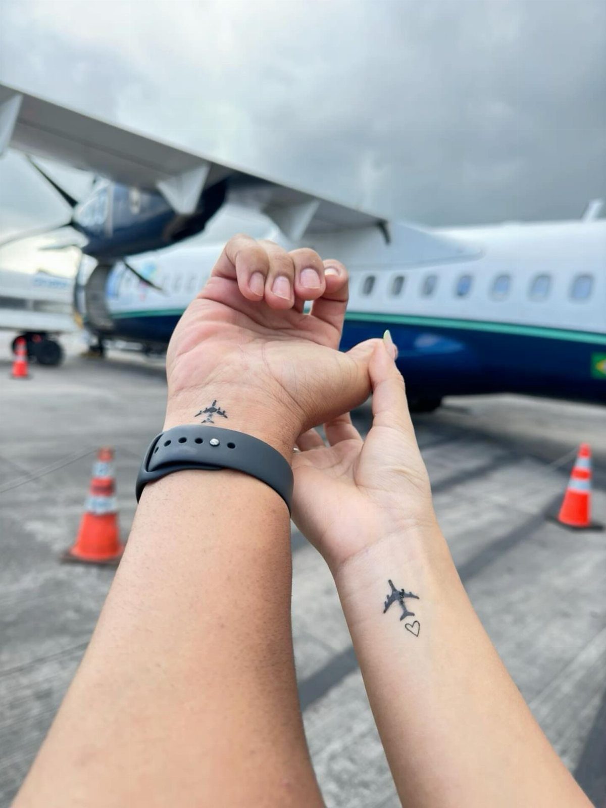 Airplane temporary tattoos on wrists with a real airplane in the background.