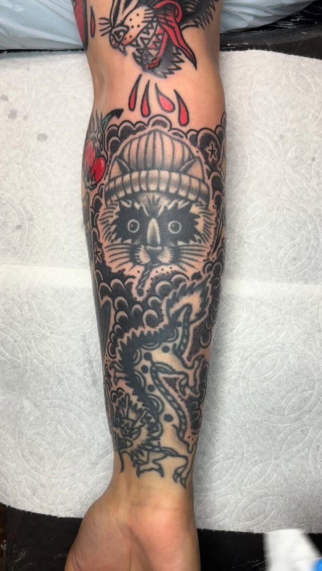 Traditional tattoos on a leg featuring a cat, dragon, and swirling cloud filler patterns.