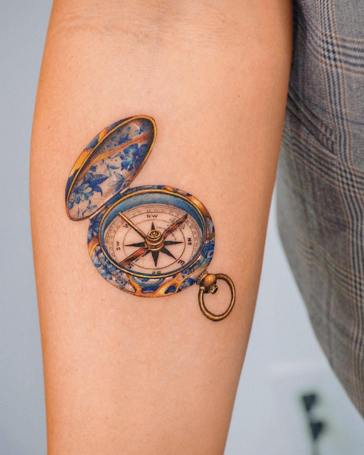 Pocket compass tattoo on an arm with gold casing and blue patterned lid.