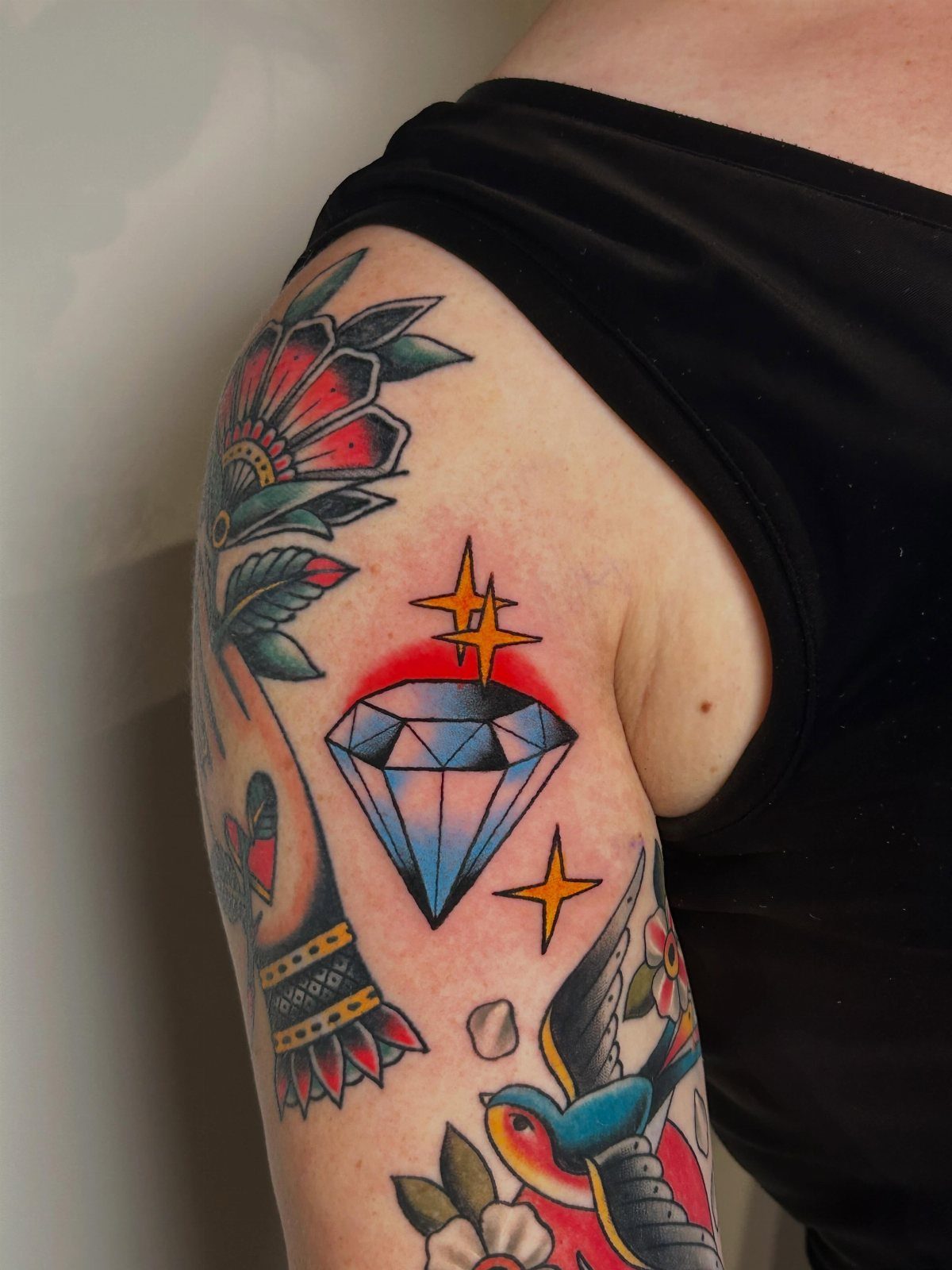 Traditional tattoo of a blue diamond with yellow sparkles on an arm.