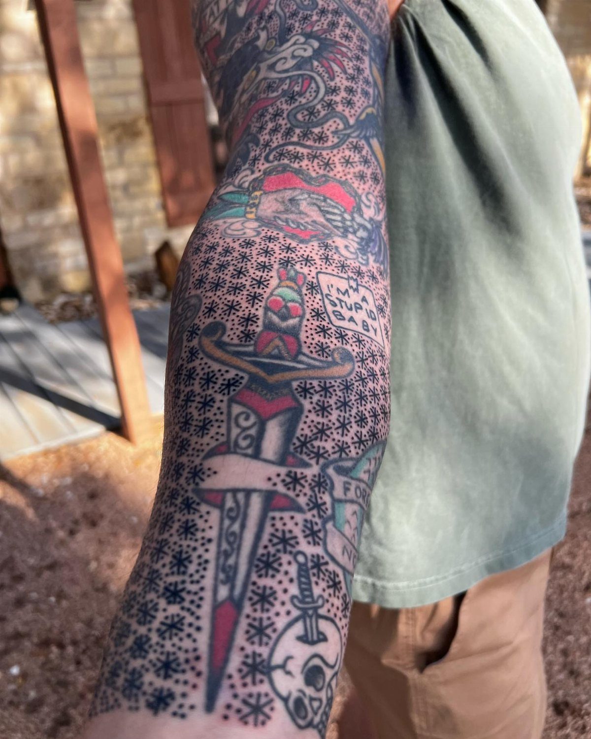 Tattooed arm with a dagger and skull surrounded by small black dot filler.