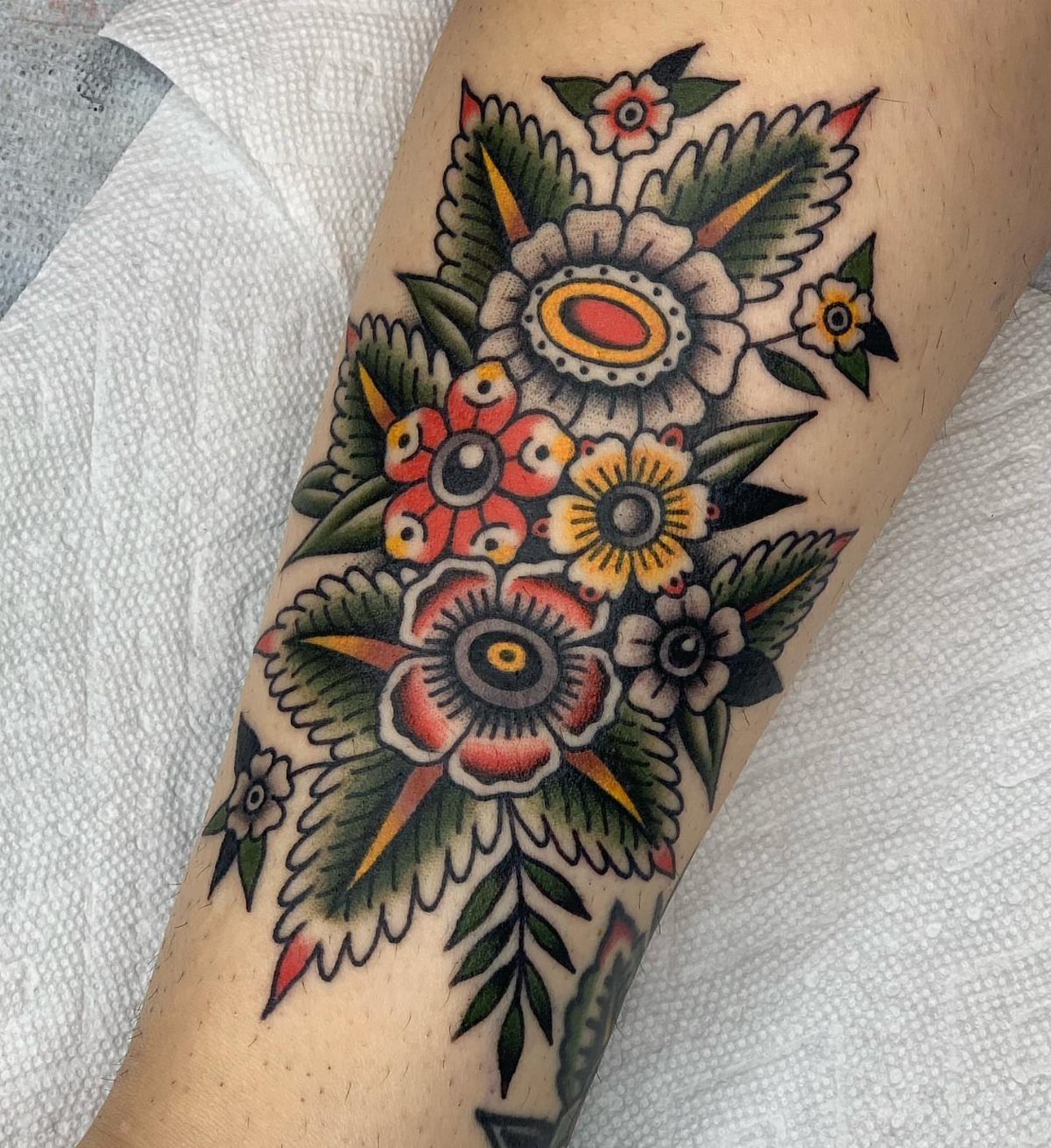 Traditional style tattoo of colorful flowers and green leaves on human skin.