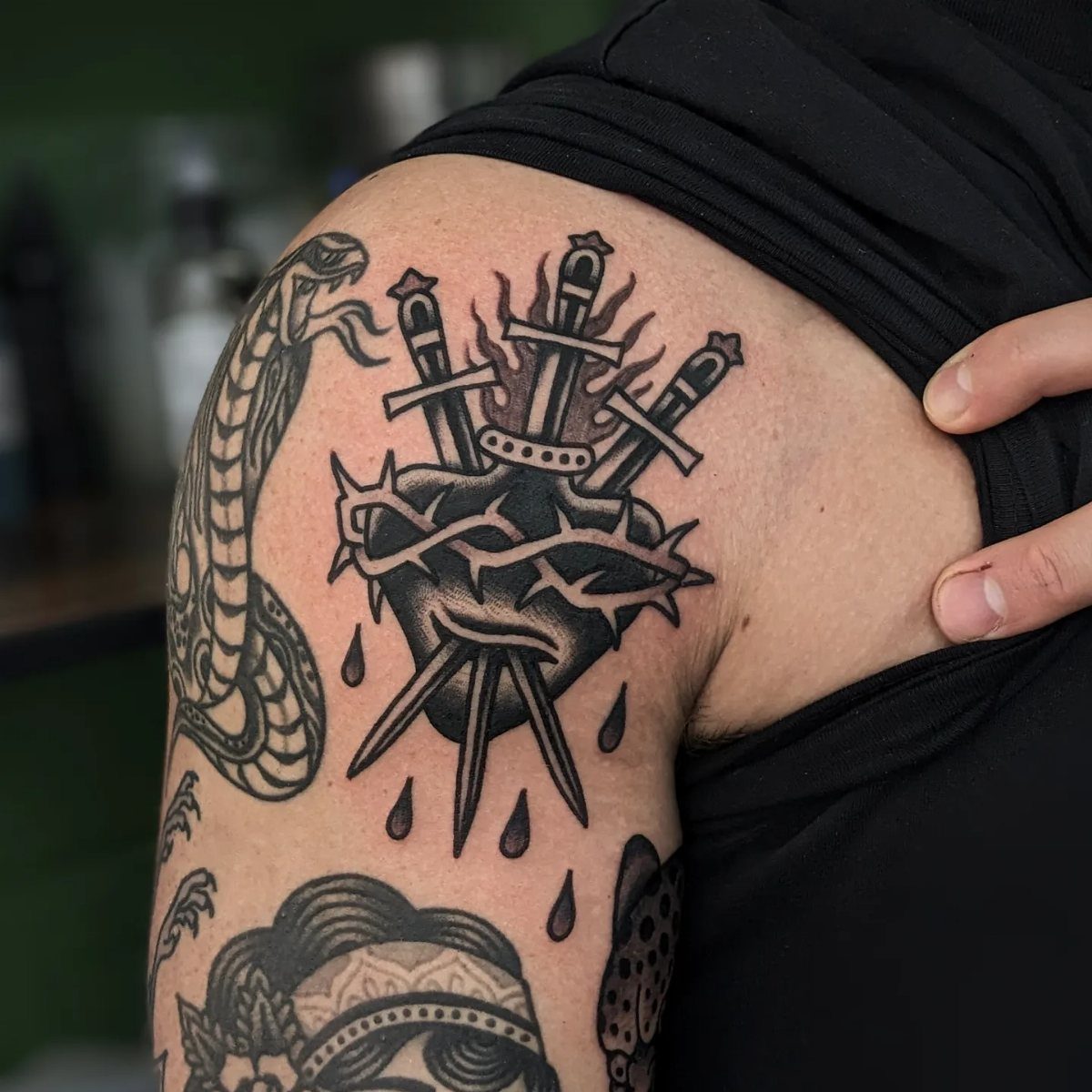 Tattoo of a heart pierced by three swords and wrapped in thorns on arm.