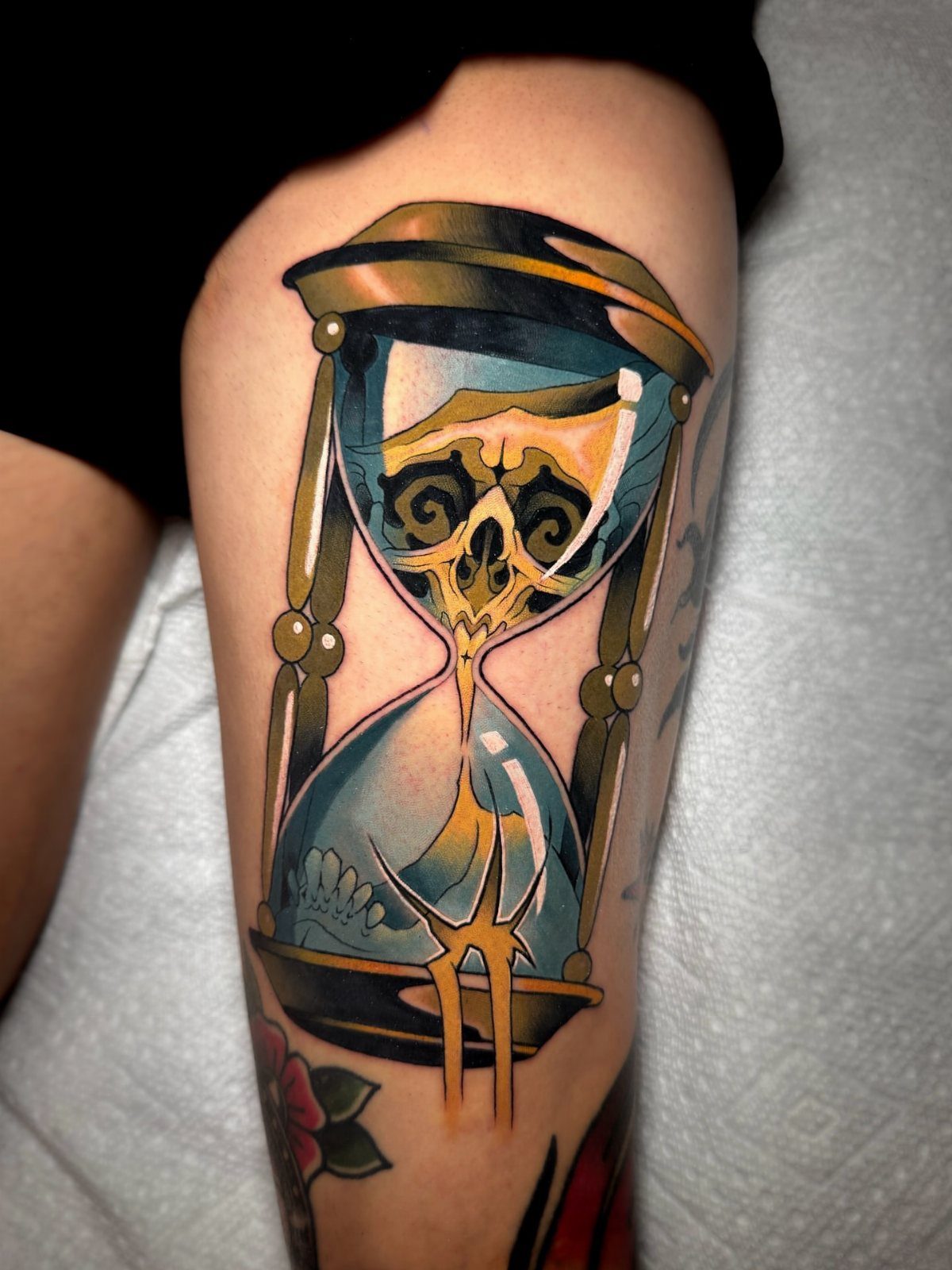 Hourglass tattoo with a skull inside on a person's leg in traditional style