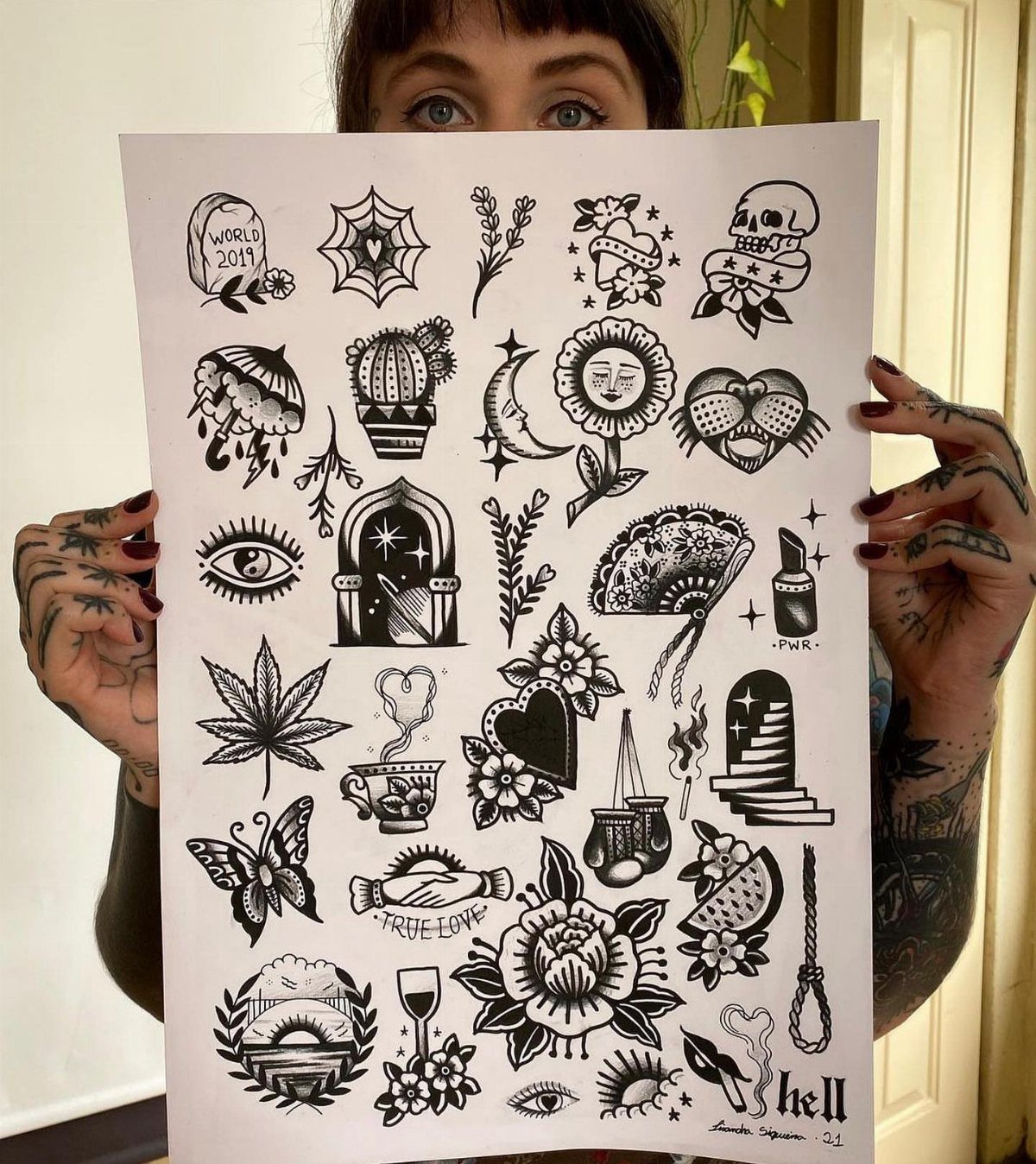 Tattoo flash sheet with various traditional black ink designs held by tattooed hands.