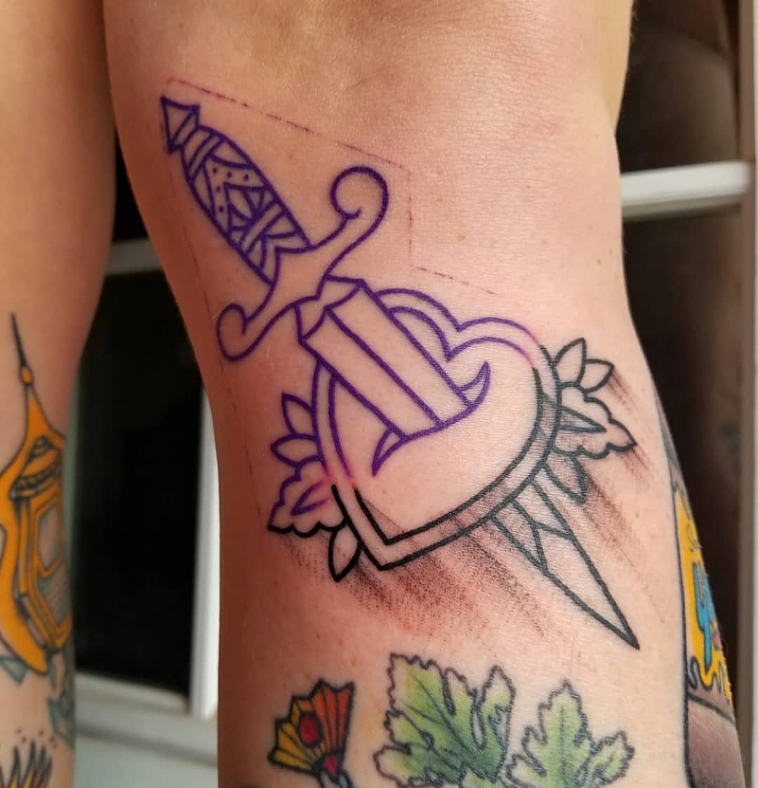 Purple ink tattoo stencil of a dagger through a heart on skin