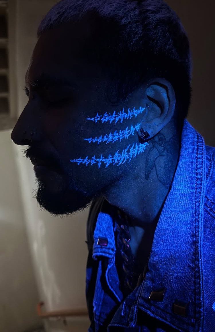 Man with glowing blue UV tattoos on his cheek under blacklight illumination.