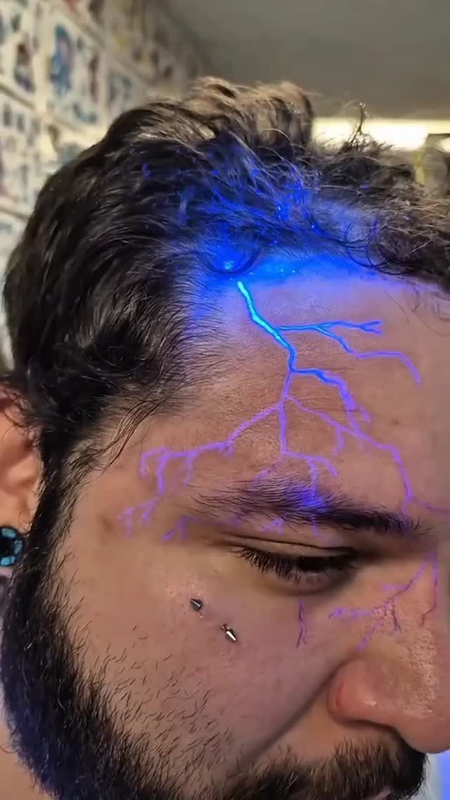 Man with a glowing blue UV lightning bolt tattoo on his forehead and cheek.