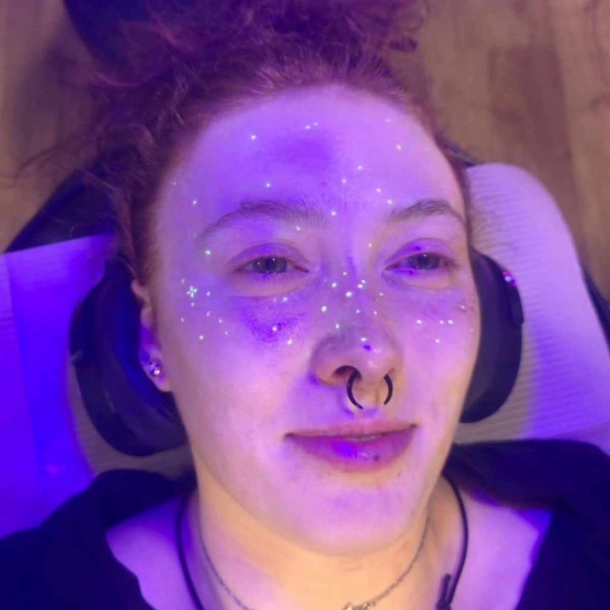 Person with glowing UV face tattoos and a septum ring under purple light.