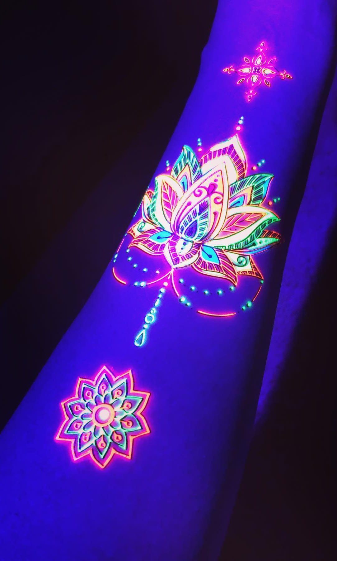 Glowing neon UV tattoos of a blossomed lotus flower on a person's arm.