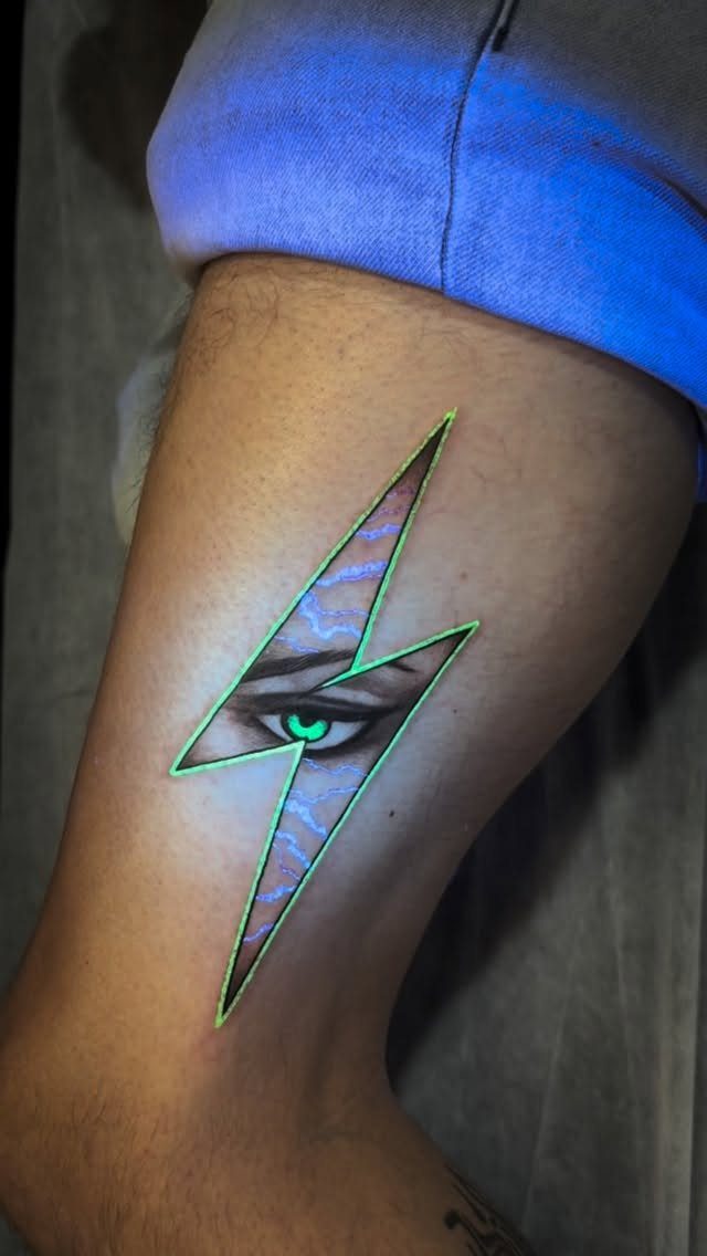 Lightning bolt UV tattoo with a glowing green outline and an eye on a leg