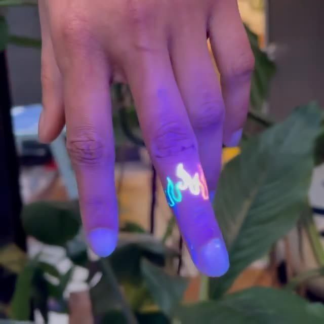 Glowing neon blue and yellow flame UV tattoo on a person's finger.