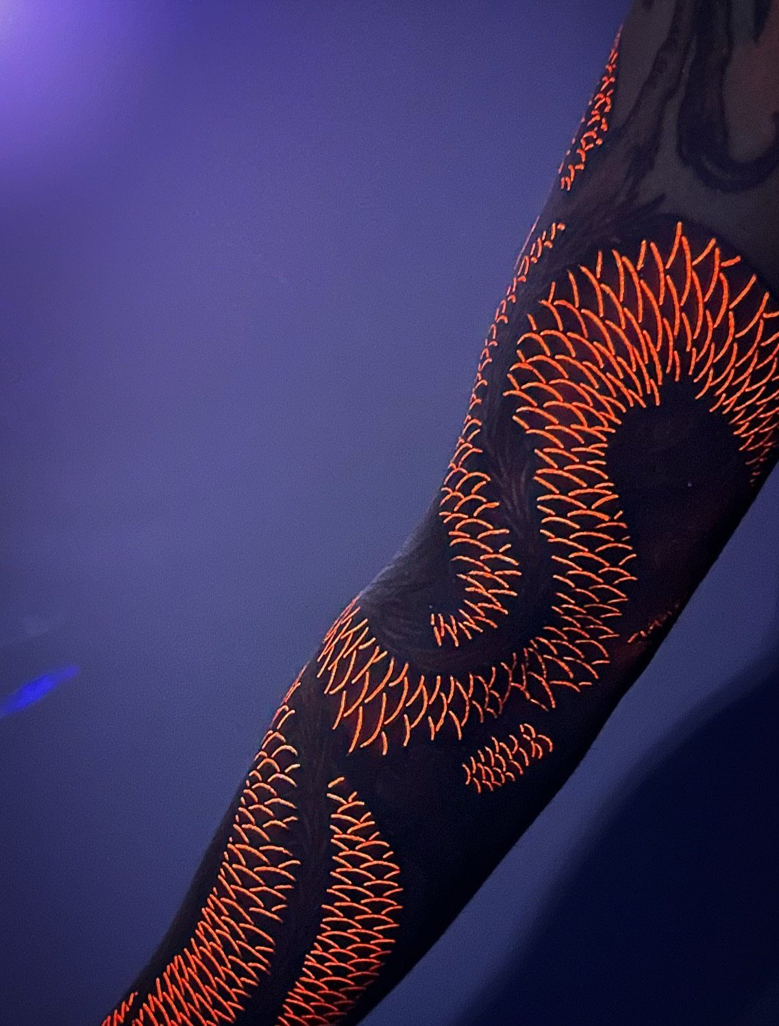 Glowing orange UV tattoo scales on a person's arm against purple background