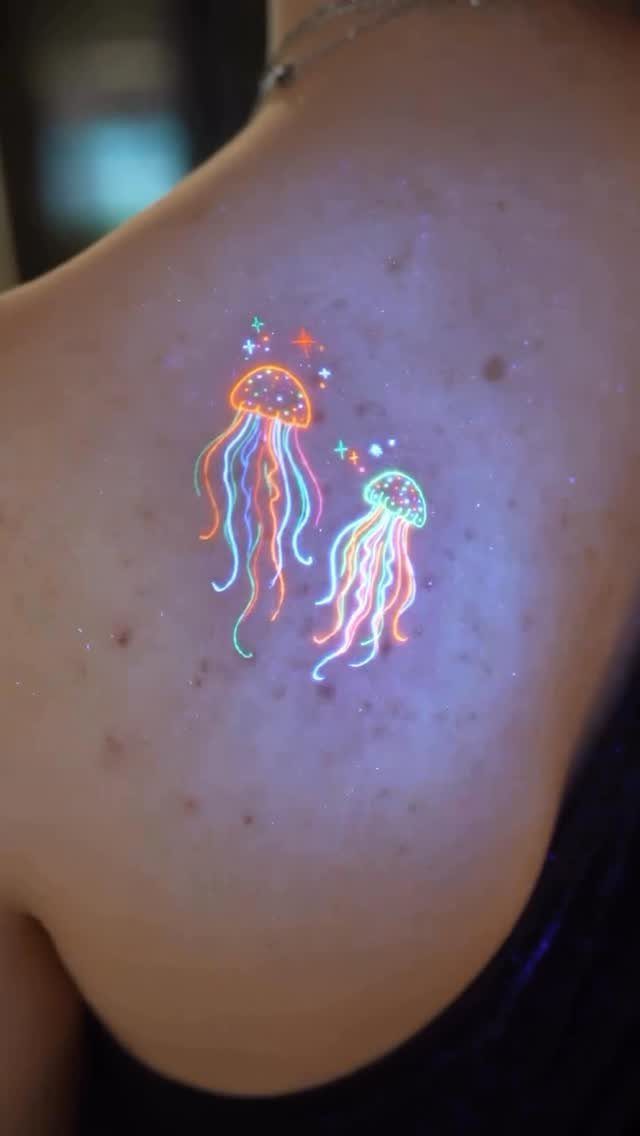 Neon jellyfish tattoos with glowing colorful tentacles on a person's shoulder.