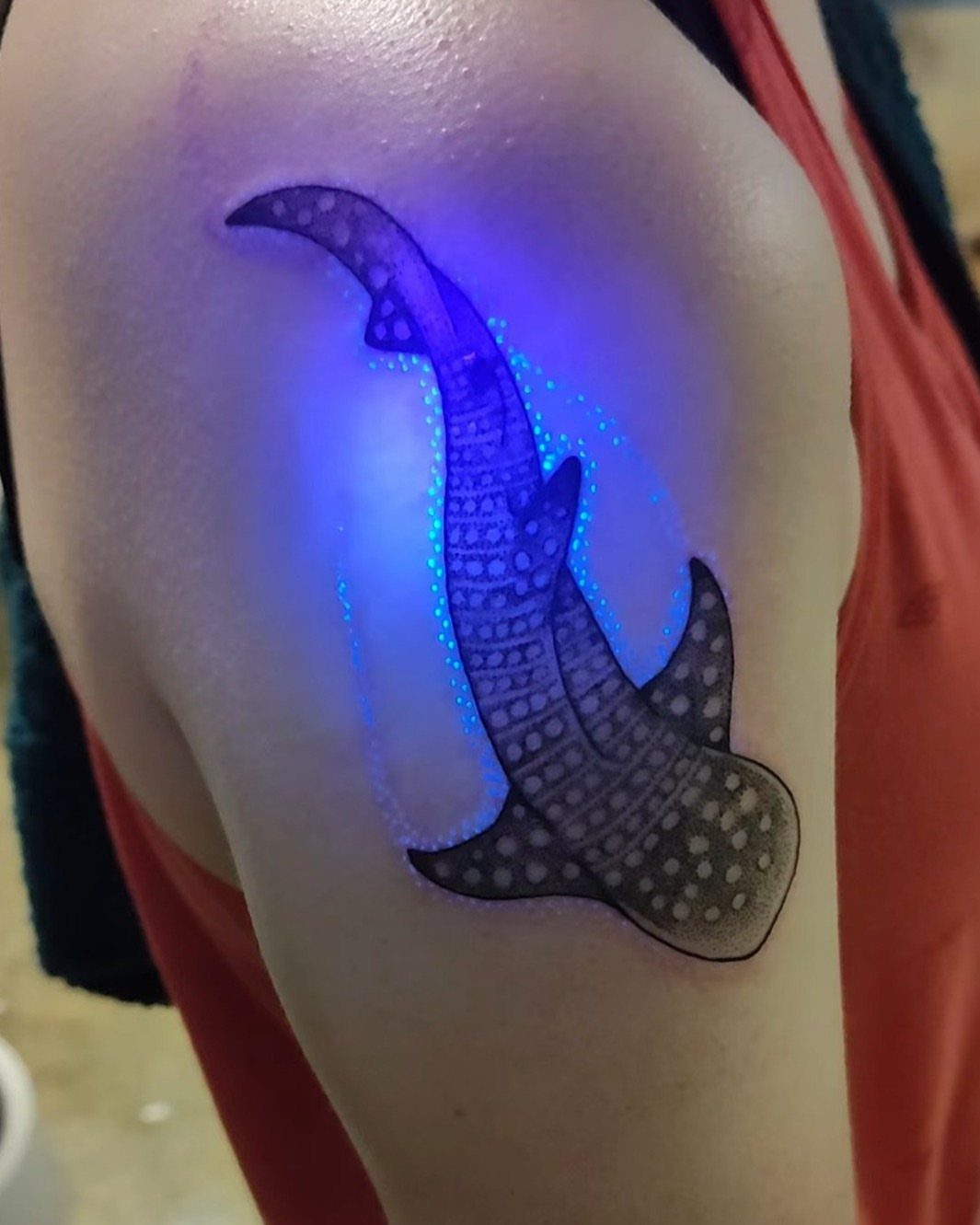 Glowing blue UV tattoo of a patterned aquatic creature on a person's arm