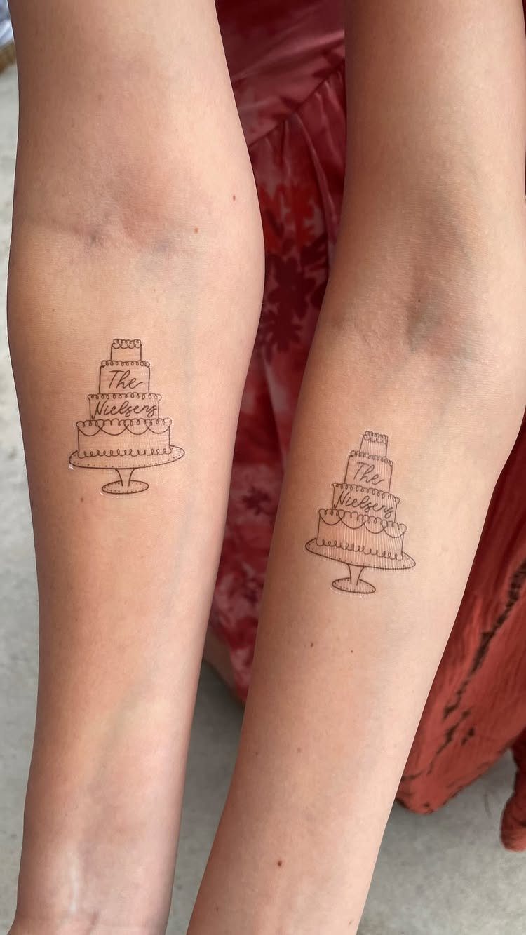 Two forearms with matching temporary tattoos of a tiered wedding cake with text.