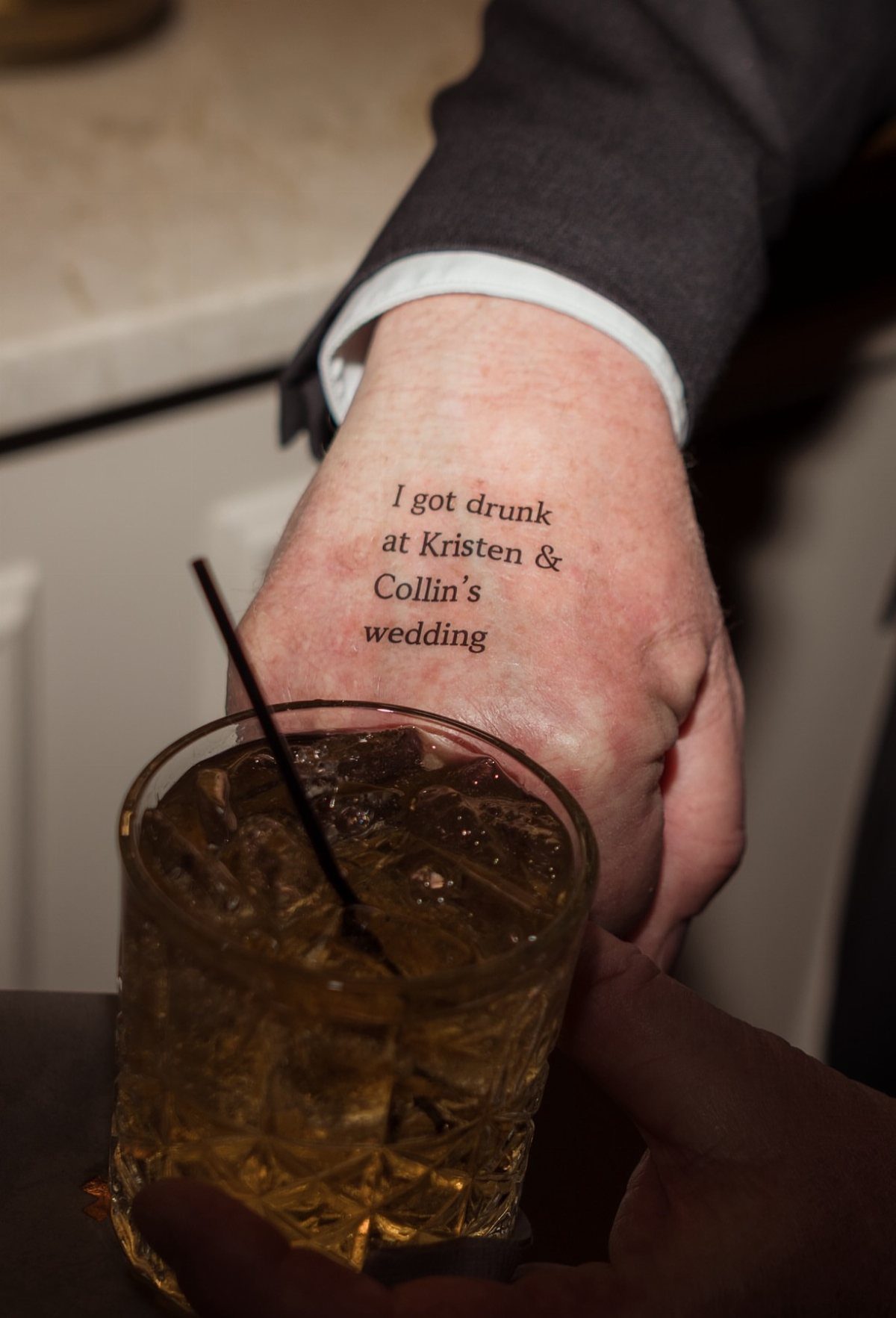 Hand with a funny wedding temporary tattoo holding a glass of whiskey with ice