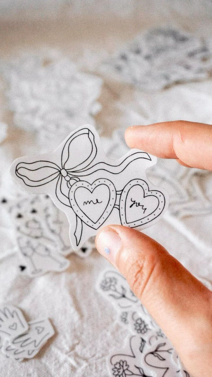 Hand holding a temporary tattoo sheet with interlocking hearts and a bow.