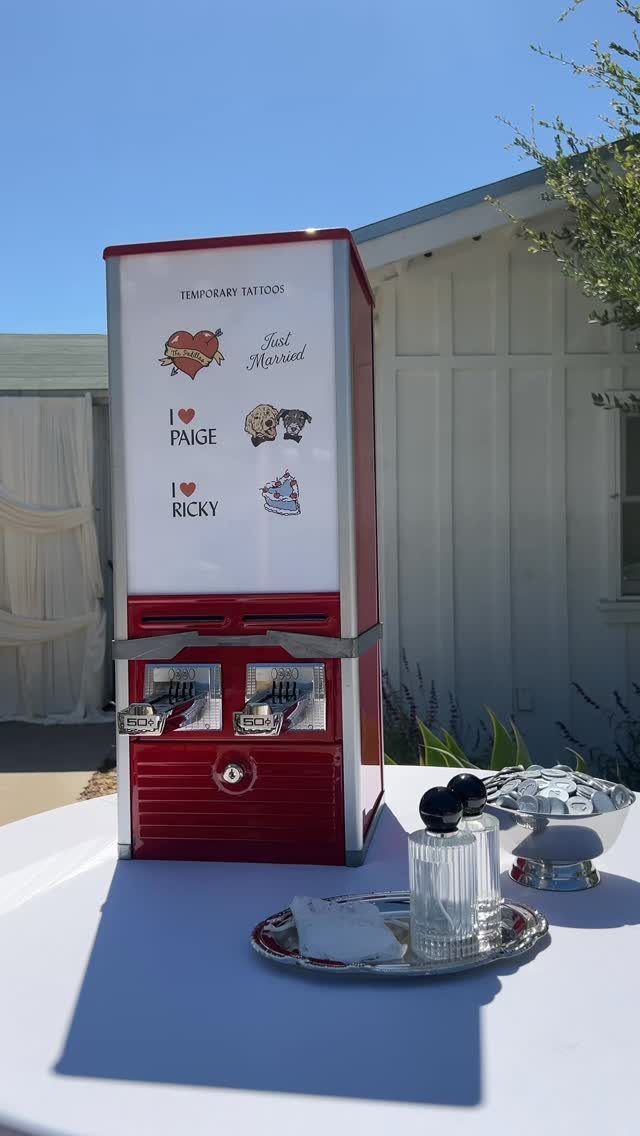 Red vintage gumball machine filled with wedding temporary tattoos on a white table.