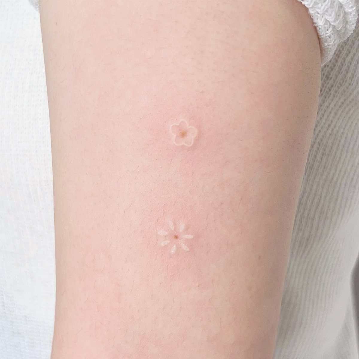 Two small white ink flower tattoos on a fair-skinned arm.