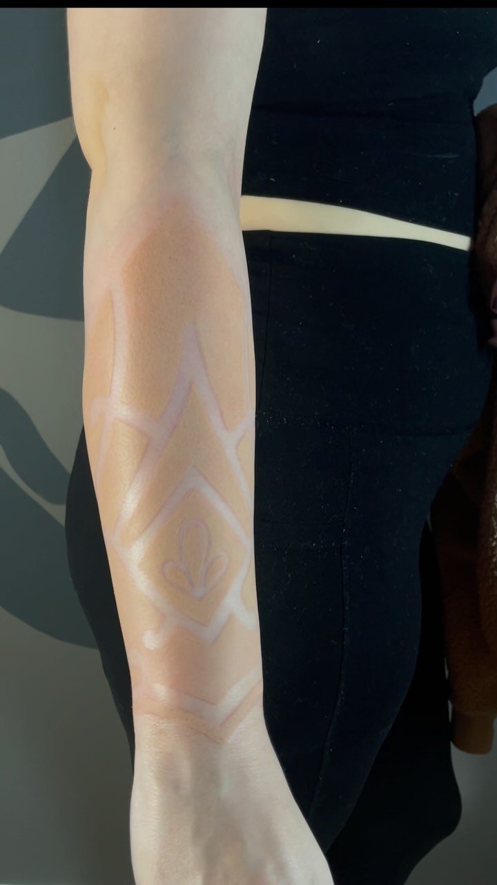 White ink tattoo with geometric diamond patterns on a person's fair forearm