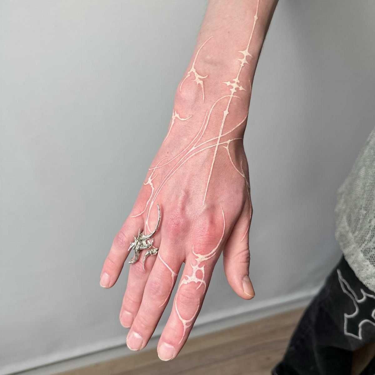 Hand and wrist with delicate white ink tattoos in an abstract organic pattern