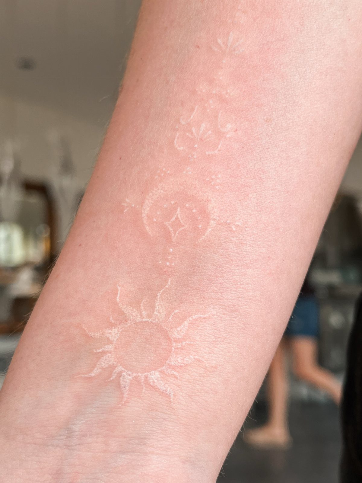 White ink tattoos of a sun and symbols on a pale forearm