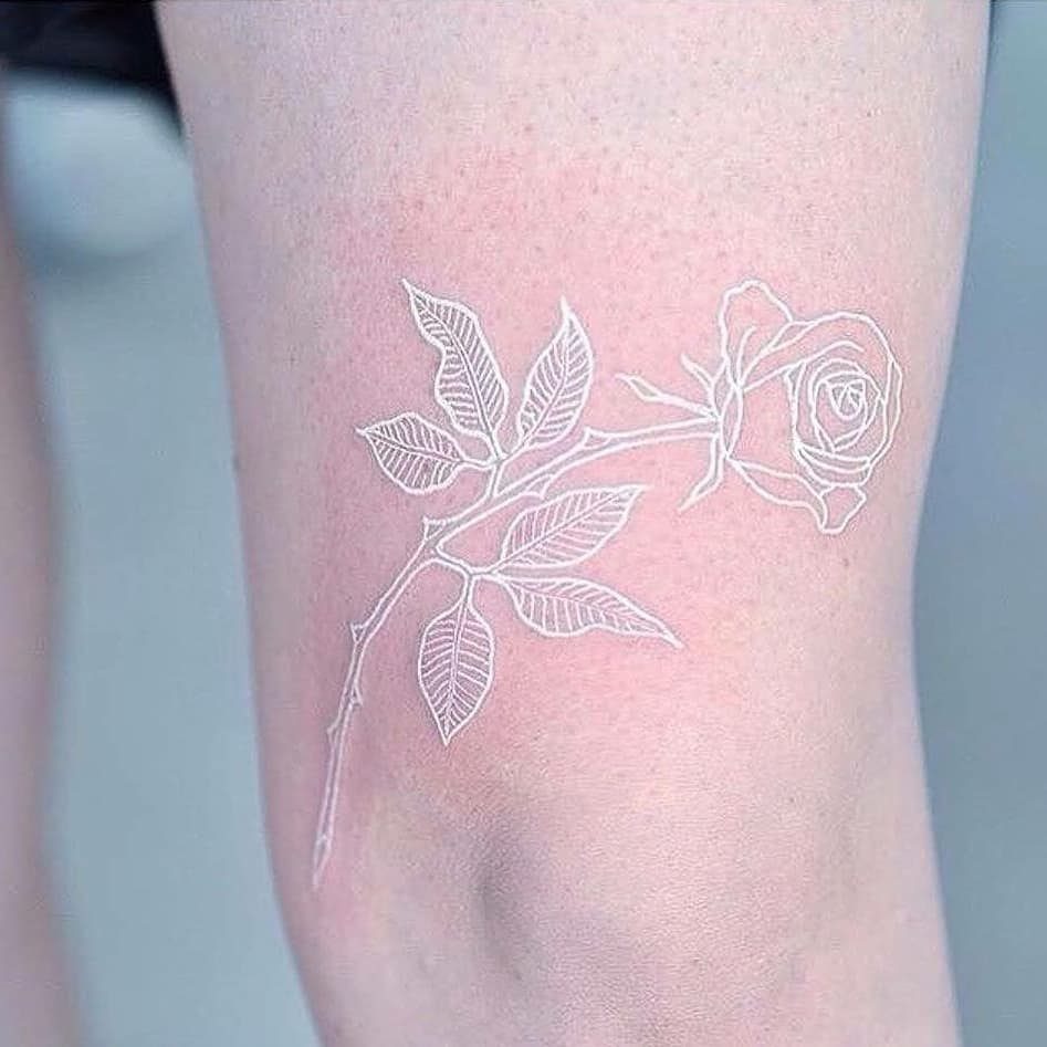 White ink rose tattoo with detailed leaves and stem on fair skin