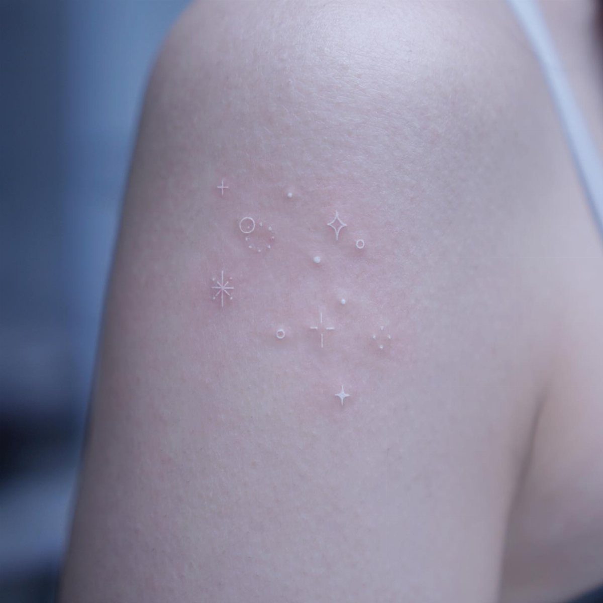 Small white ink star and sparkle tattoos on a person's upper arm.