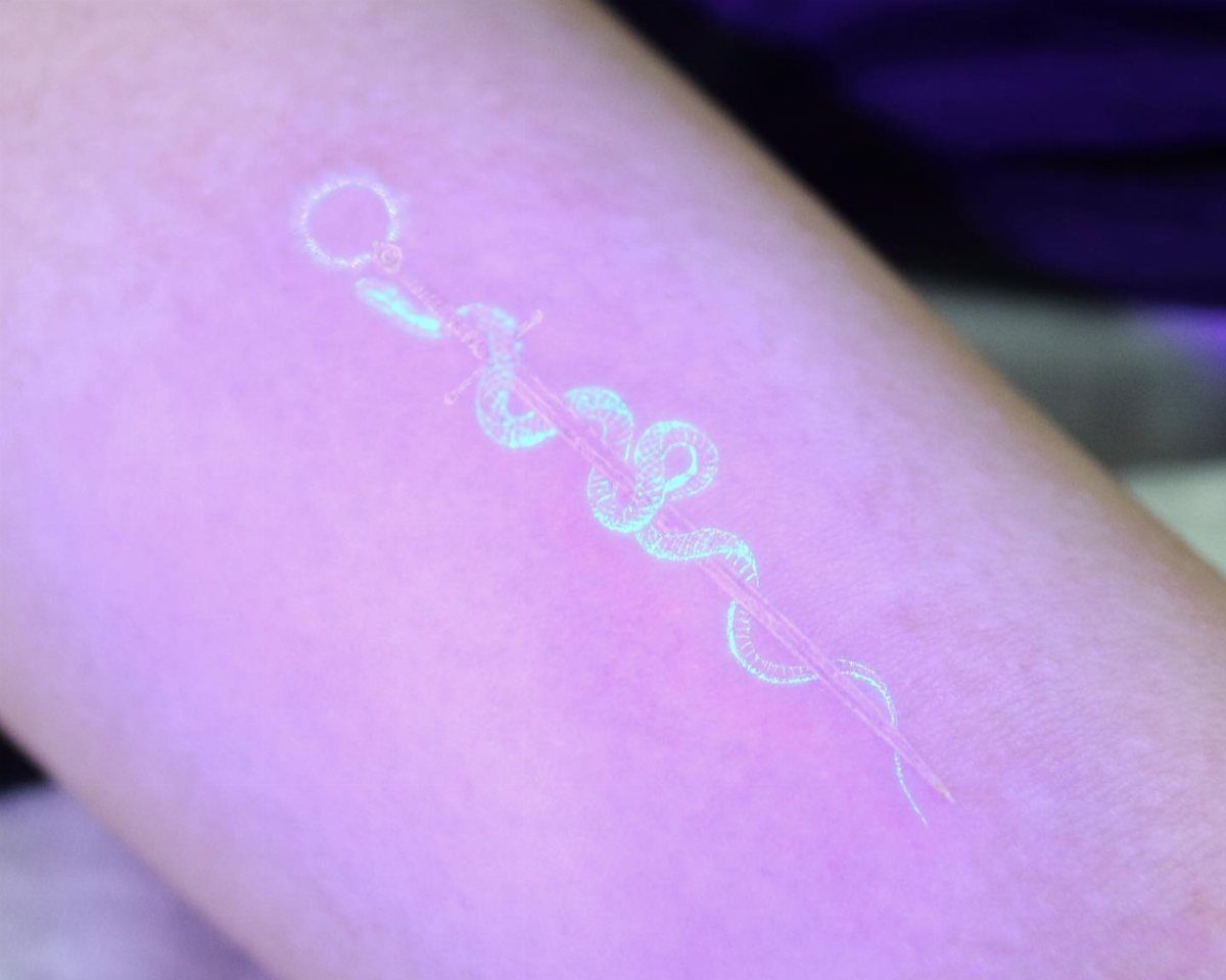 Glowing white UV tattoo of a snake wrapped around a sword on an arm.