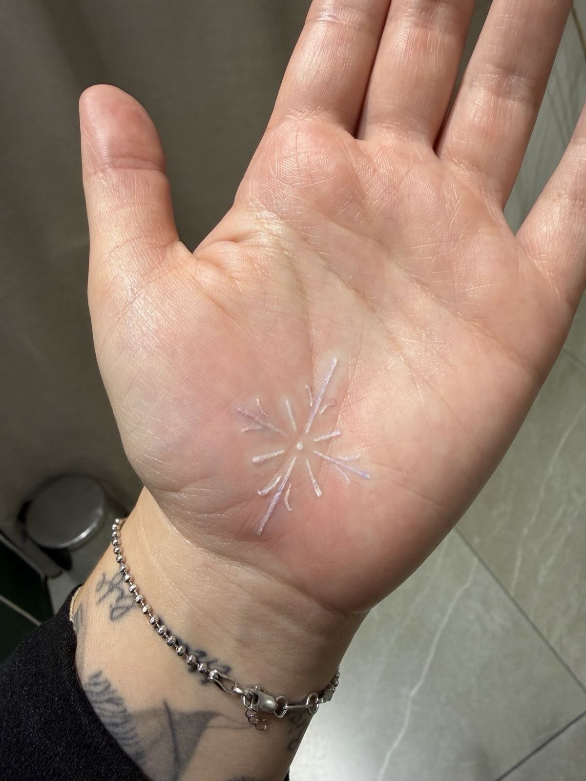 White ink snowflake tattoo centered on the palm of a person's hand
