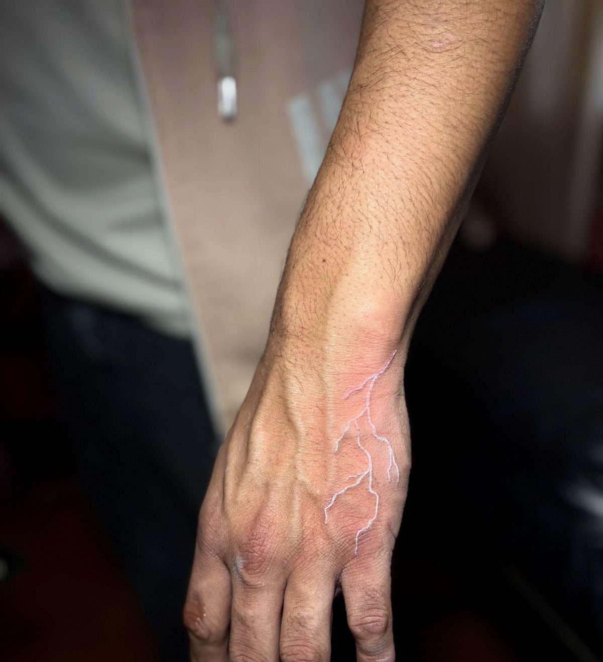 White ink branching lightning bolt tattoo on the back of a hand.