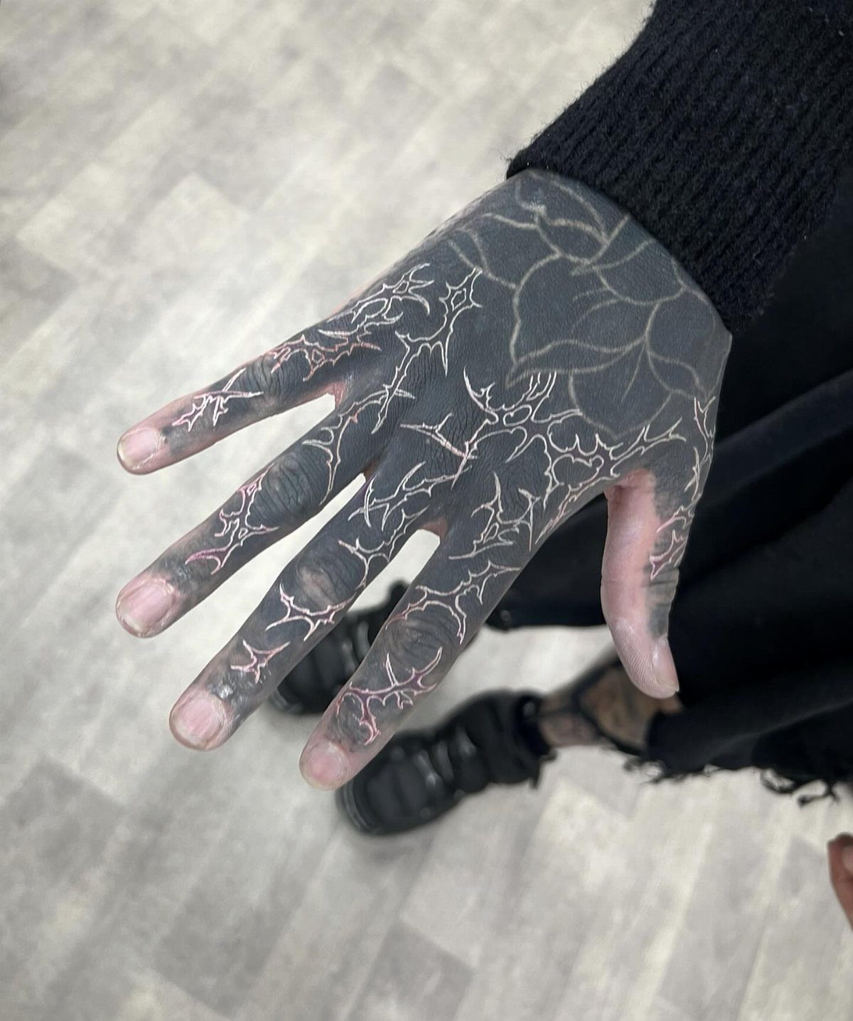 Hand with black ink tattoos and white ink lightning bolt patterns on fingers.