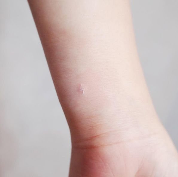 Small white ink lightning bolt tattoo on a person's ankle.