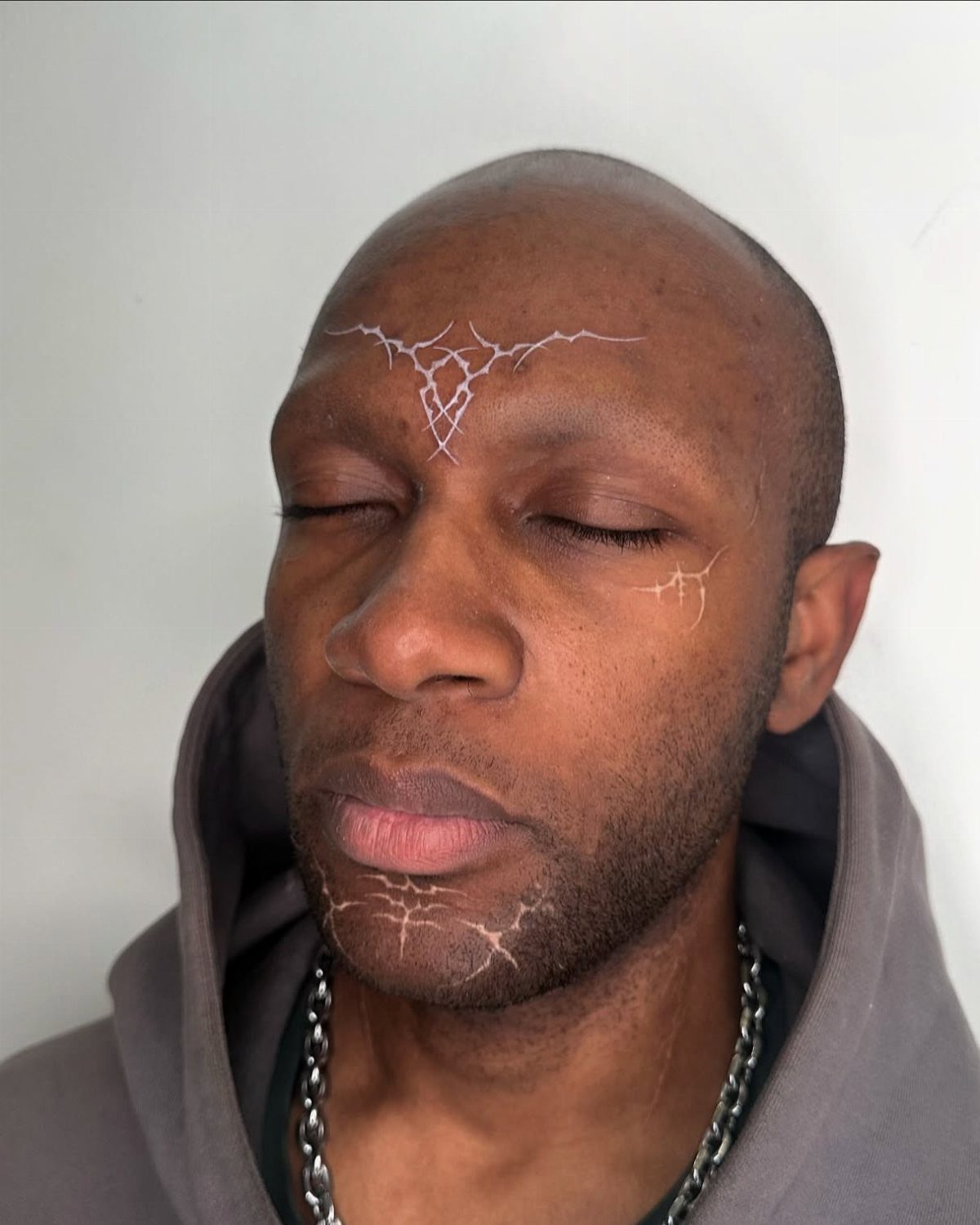 Man with dark skin featuring white ink lightning bolt tattoos on his face