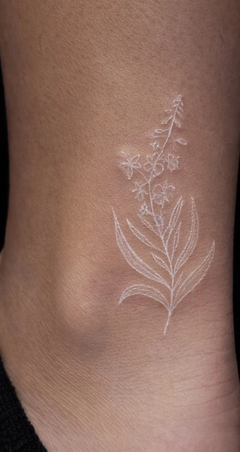 White ink floral tattoo on dark skin located on the ankle area.