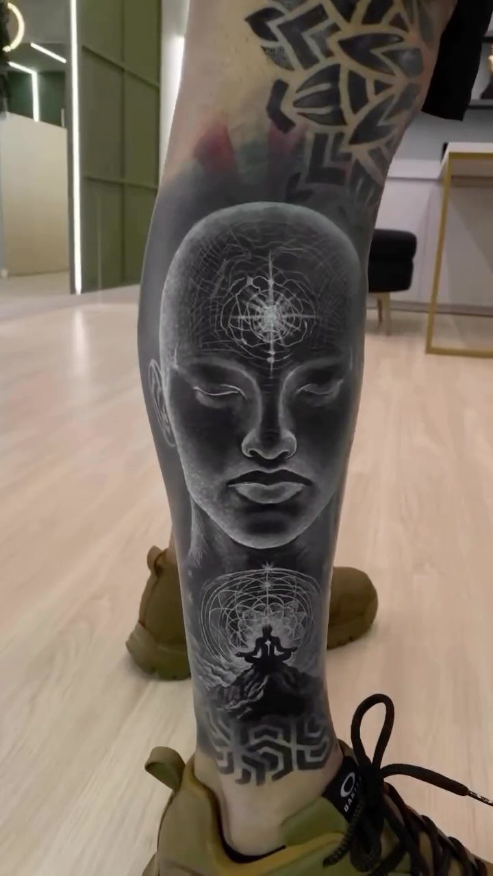 Geometric white ink tattoo of a face and figures on a lower leg.
